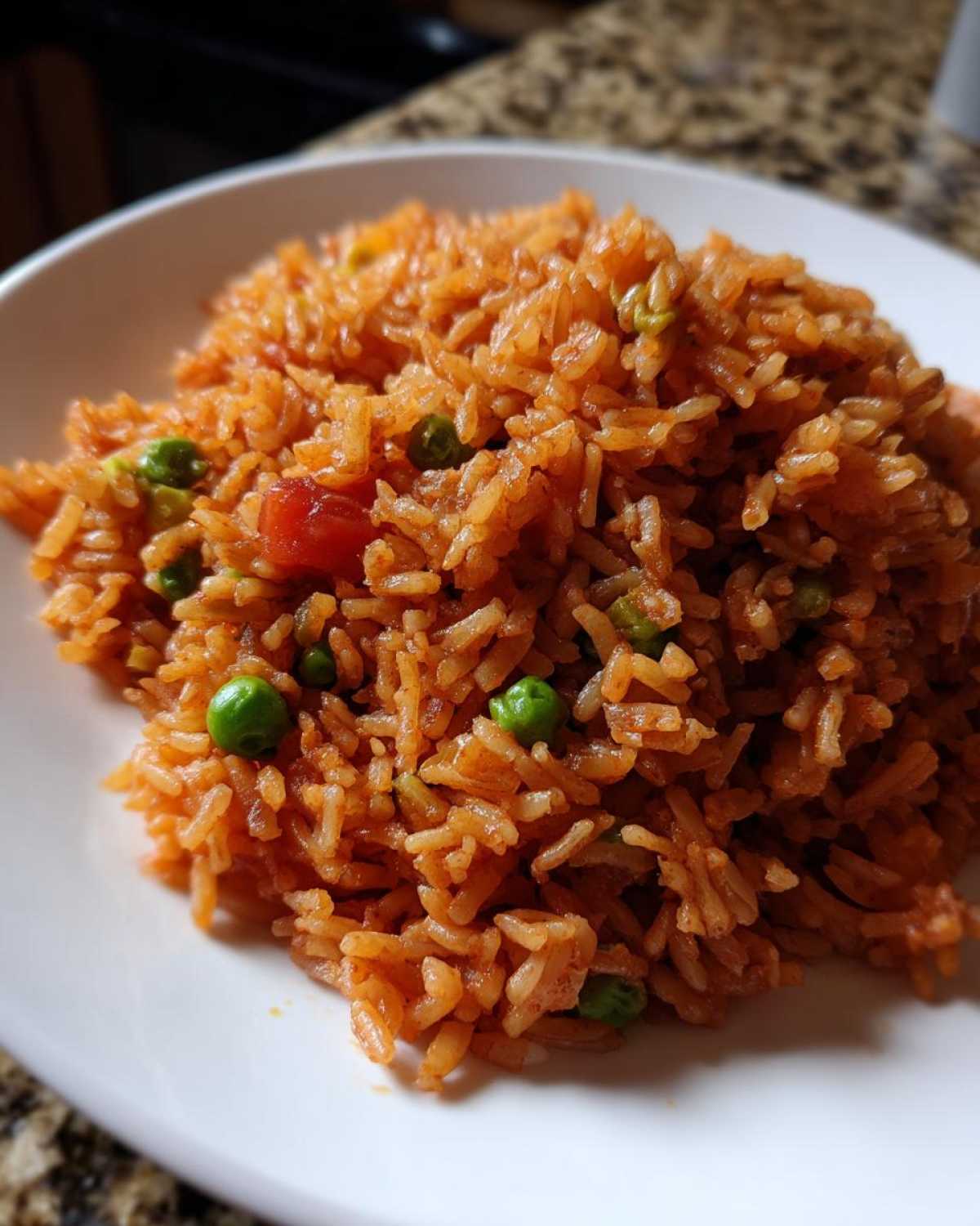 A close-up of bright orange spanish rice mixed with green peas and diced tomato served on a white plate.