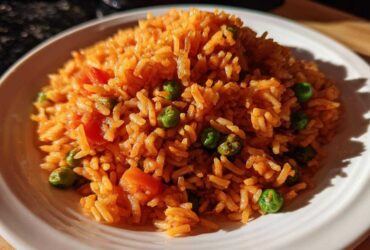 A close-up of a mound of vibrant orange Spanish rice mixed with bright green peas and diced tomatoes on a white plate.
