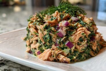 A mound of creamy salmon salad mixed with greens and red onion, topped with fresh dill.