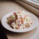 A mound of creamy, flavorful crab salad with visible celery and red onion pieces on a white plate.