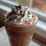 A tall glass of rich, blended frozen hot chocolate topped with whipped cream and chocolate shavings.