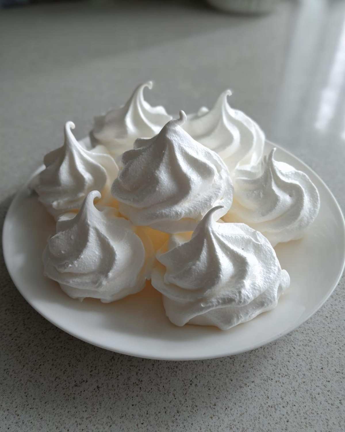 A close-up of several perfectly piped white meringue cookies arranged on a white plate.
