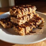 A stack of homemade, chewy protein bars made with oats and drizzled generously with melted dark chocolate.