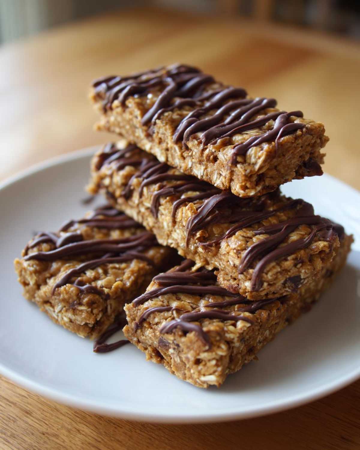 A stack of four homemade, oat-based protein bars drizzled generously with melted dark chocolate.
