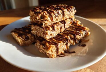 A stack of homemade, chewy protein bars made with oats and drizzled generously with melted dark chocolate.