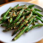Close-up of bright green beans tossed with toasted breadcrumbs and seasoning on a white plate.