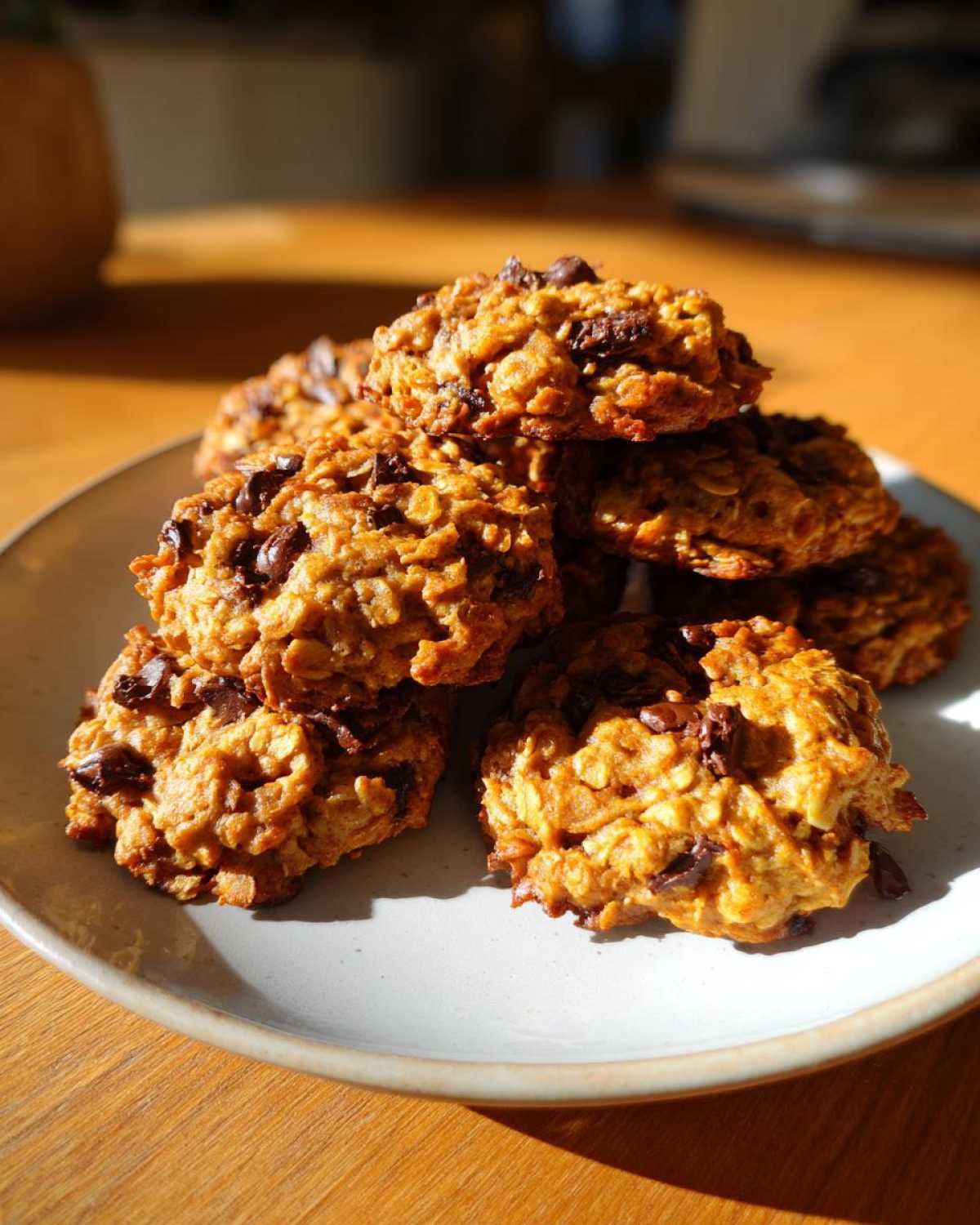 A stack of freshly baked, golden brown oatmeal cookie treats loaded with chocolate chips on a light plate.