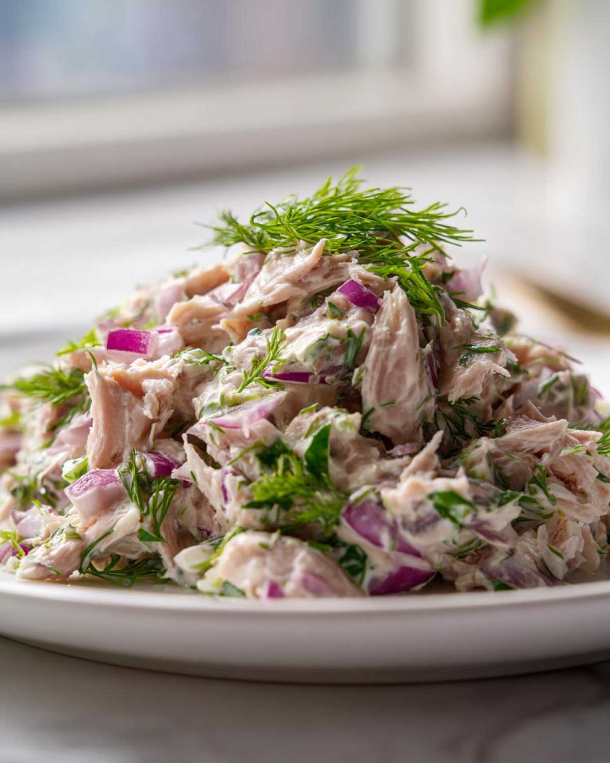 Close-up of a mound of creamy salmon salad mixed with bright purple red onion chunks and fresh dill.