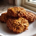 A stack of four golden brown, textured breakfast cookie oat clusters resting on a white plate.