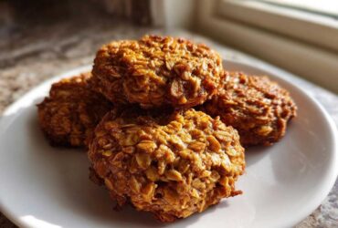A stack of four golden brown, textured breakfast cookie oat clusters resting on a white plate.