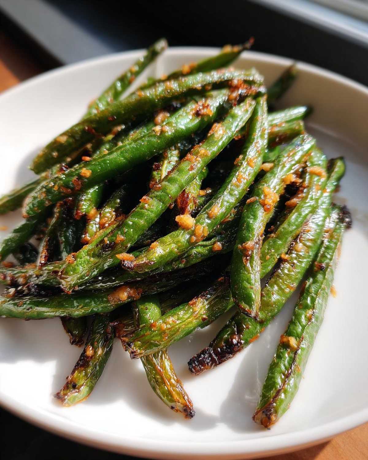 Close-up of blistered and seasoned green beans piled on a white plate, highlighting the texture of the cooked green beans.