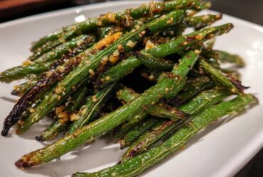 A close-up of perfectly cooked, slightly charred green beans seasoned with minced garlic served on a white plate.