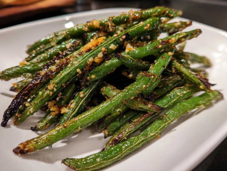 A close-up of perfectly cooked, slightly charred green beans seasoned with minced garlic served on a white plate.