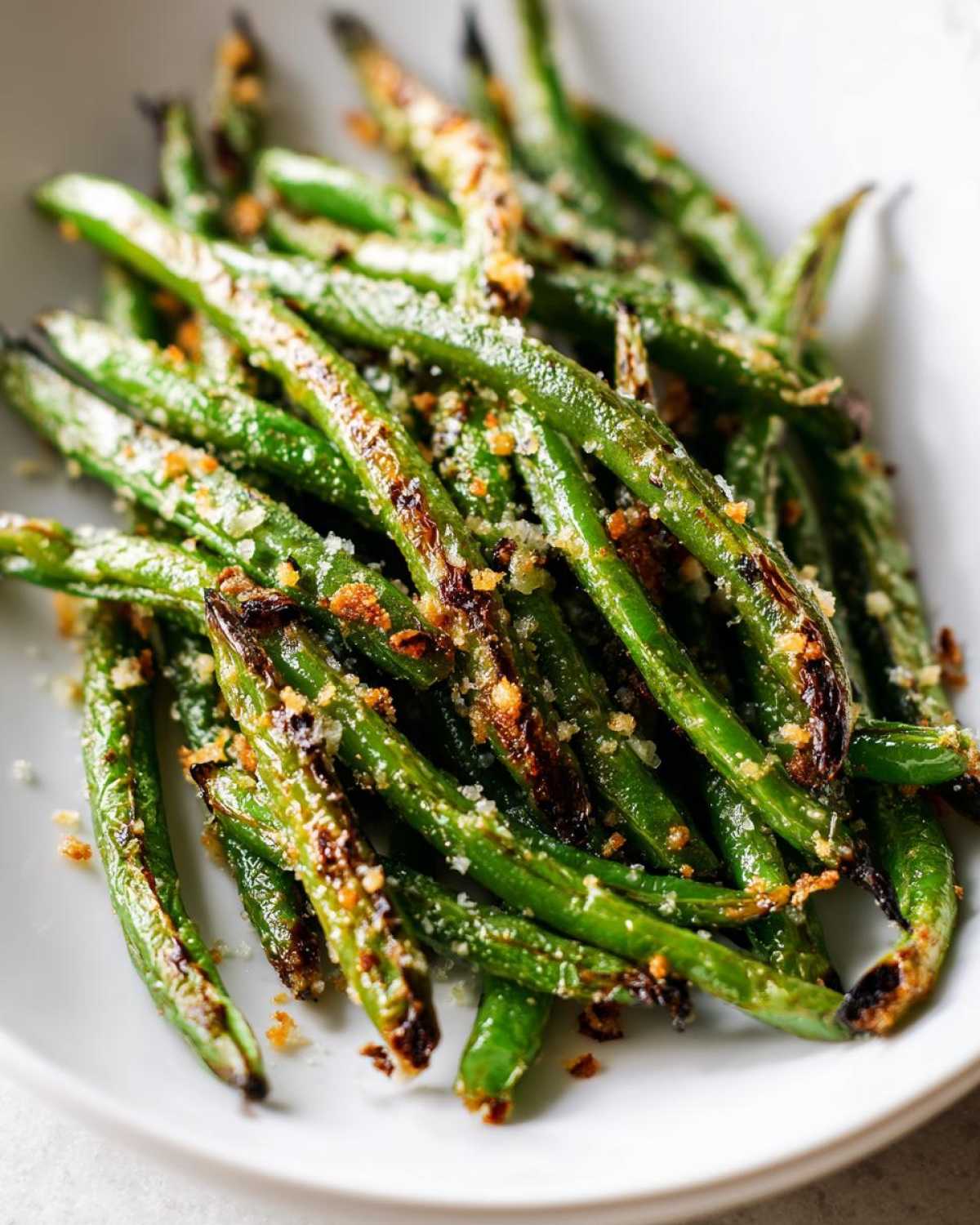 Close-up of bright green beans roasted until slightly charred and topped with grated parmesan cheese and breadcrumbs.