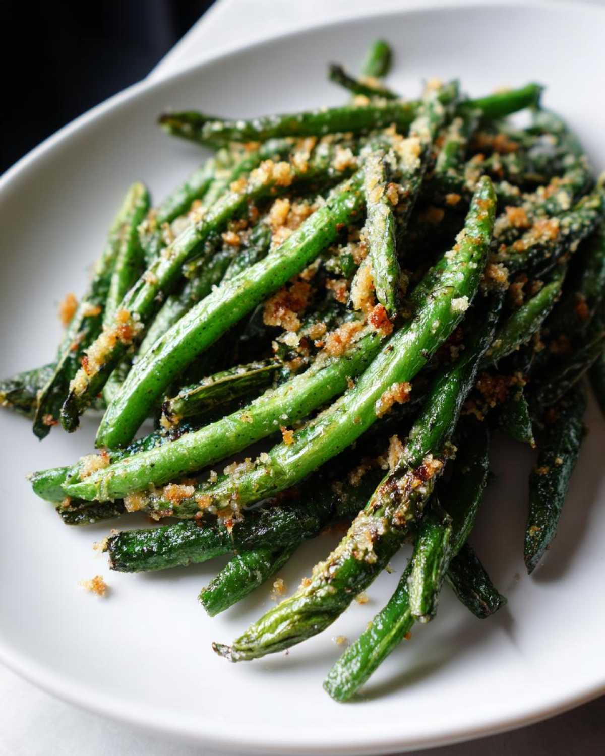 Close-up of bright green beans topped with crispy, golden breadcrumbs served on a white plate.