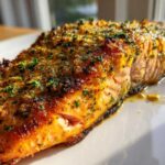 Close-up of a perfectly cooked, golden-brown air fryer salmon fillet topped with herbs.