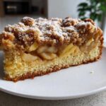 A generous slice of amazing apple crumb cake, showing layers of moist cake, spiced apples, and a thick, sugary crumb topping.