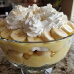 Close-up of layered banana pudding in a glass bowl, topped with whipped cream and sliced bananas.