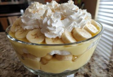 Close-up of layered banana pudding in a glass bowl, topped with whipped cream and sliced bananas.