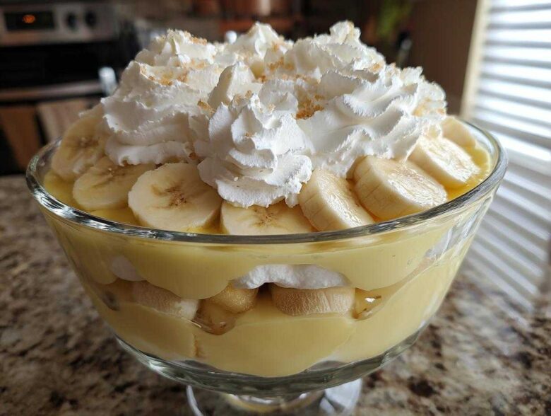 Close-up of layered banana pudding in a glass bowl, topped with whipped cream and sliced bananas.