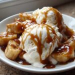 Close-up of warm, caramelized bananas foster served over scoops of vanilla ice cream drizzled with rich caramel sauce.