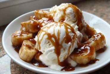 Close-up of warm, caramelized bananas foster served over scoops of vanilla ice cream drizzled with rich caramel sauce.