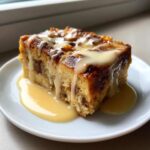 A close-up of a square slice of amazing bread pudding topped with thick vanilla sauce.