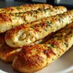 Close-up of several golden, cheesy garlic breadsticks topped with parsley, ready to eat.