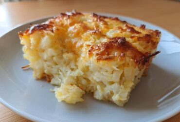 A close-up slice of amazing cheesy potato casserole with a golden-brown, bubbly cheese crust.