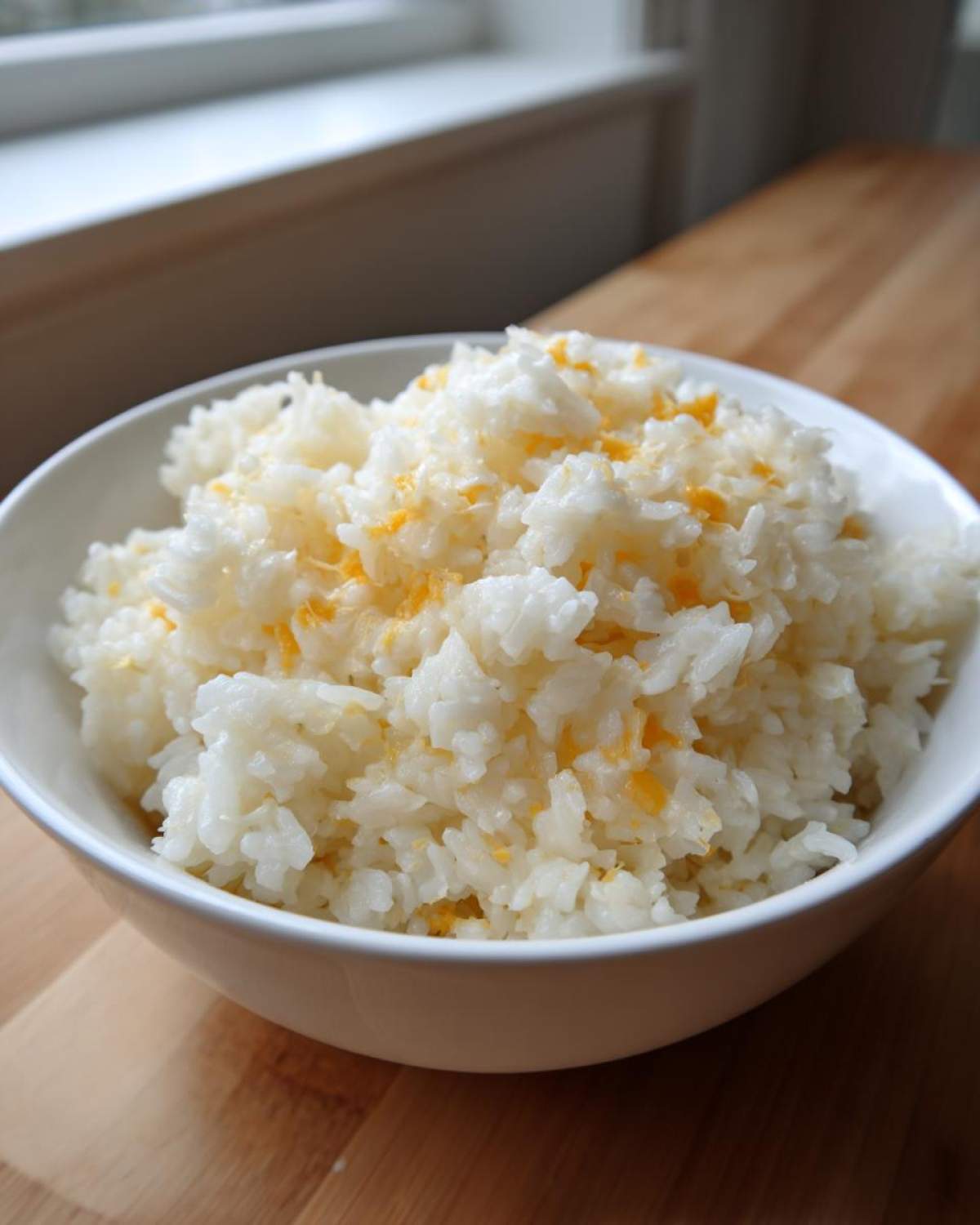 A white bowl filled with fluffy white rice topped with melted yellow cheddar for amazing cheesy rice.