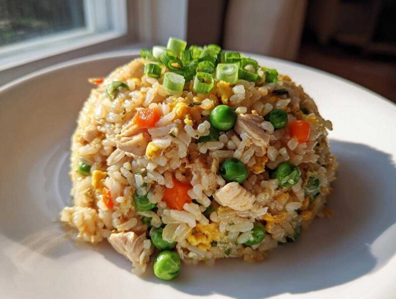 A perfectly molded mound of amazing chicken fried rice featuring visible pieces of chicken, peas, carrots, and egg, topped with green onions.