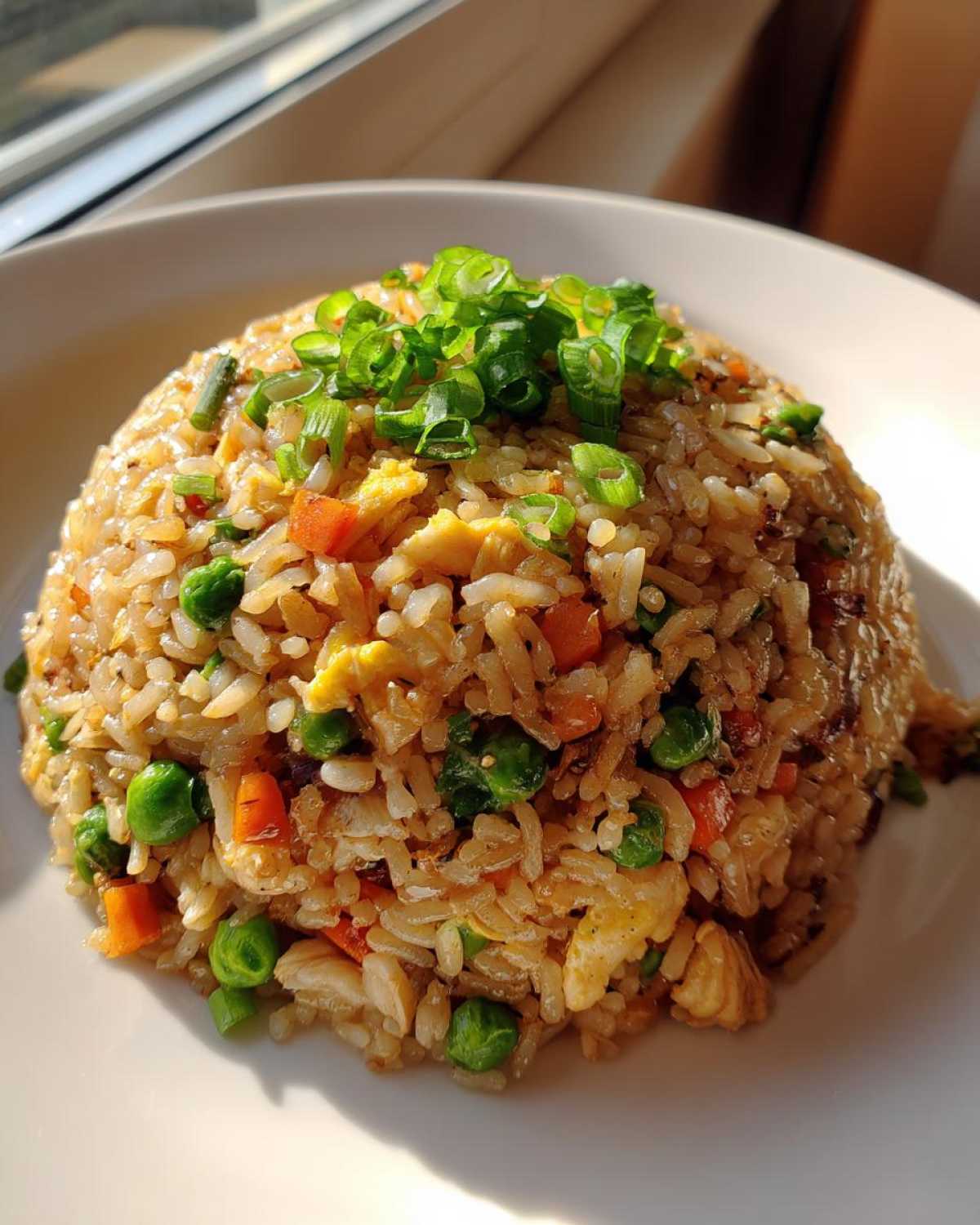 A mound of flavorful chicken fried rice mixed with peas and carrots, topped with fresh green onions.