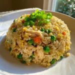A dome-shaped serving of homemade chicken fried rice with visible shredded chicken, peas, carrots, and egg, topped with fresh green onions.