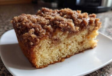 Close-up of a moist slice of coffee cake featuring a thick, sugary cinnamon crumb topping on a white plate.