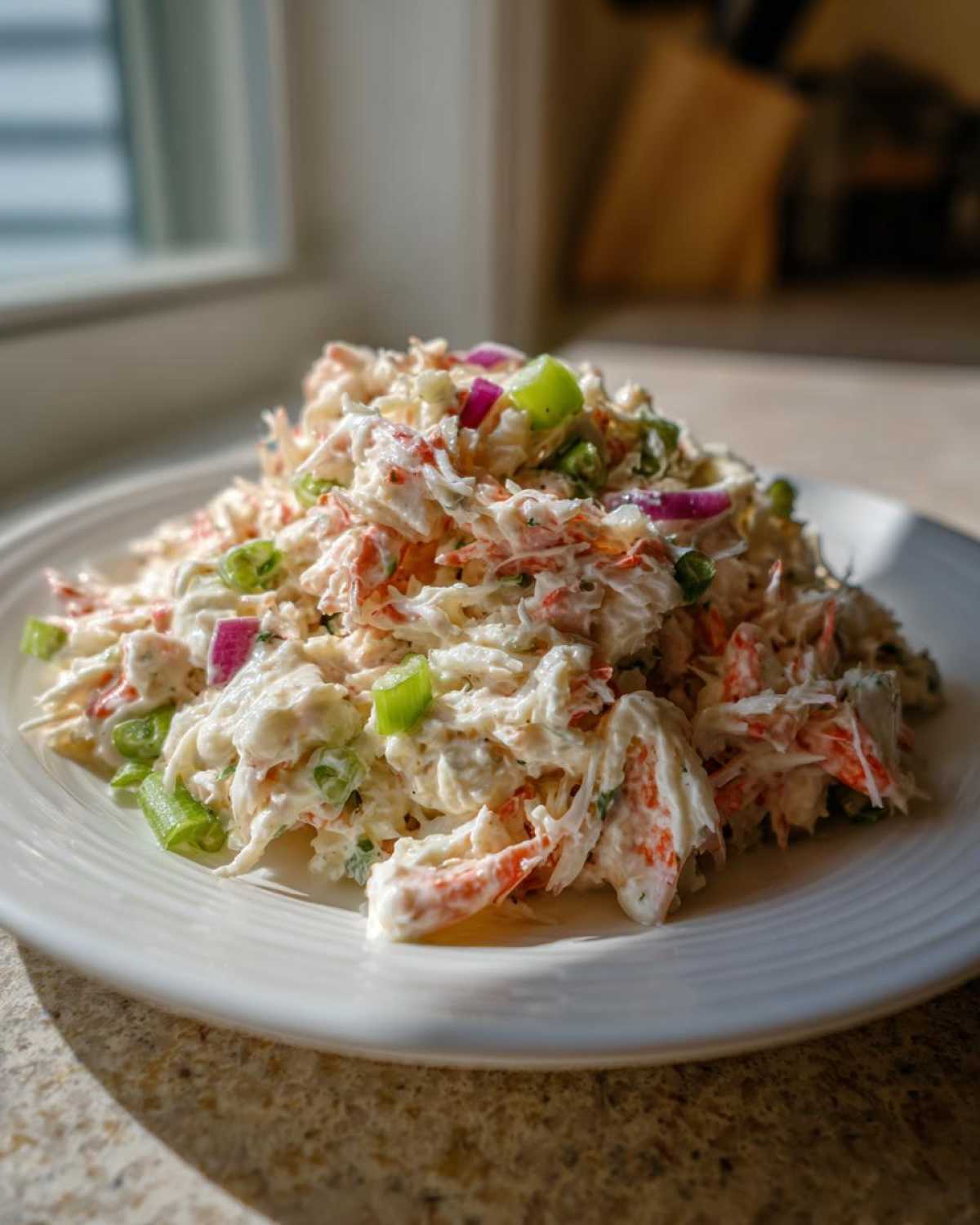 A generous serving of creamy crab salad mixed with celery and red onion on a white plate.