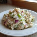 A generous scoop of creamy crab salad mixed with visible chunks of celery and red onion on a white plate.