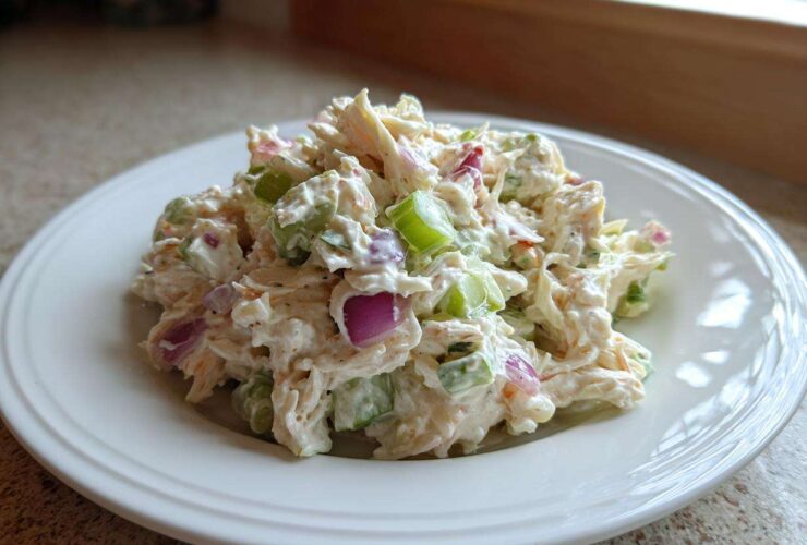 A generous scoop of creamy crab salad mixed with visible chunks of celery and red onion on a white plate.
