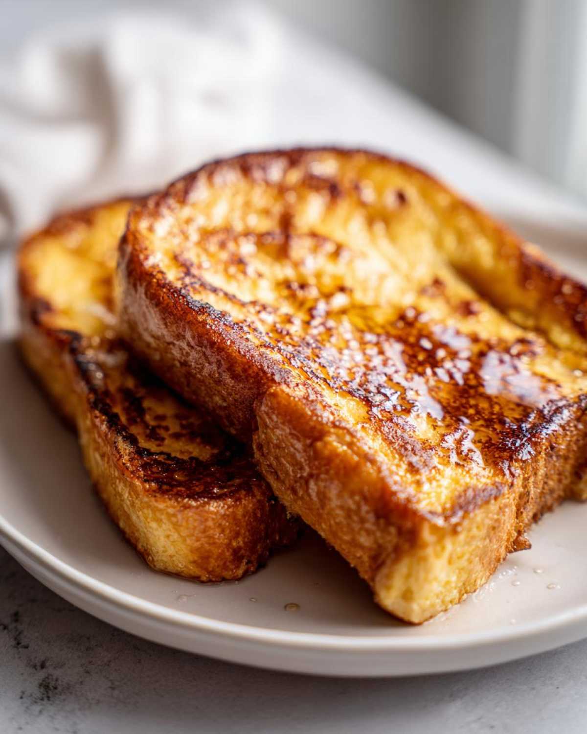 Close-up of three thick slices of golden brown french toast drizzled with syrup.