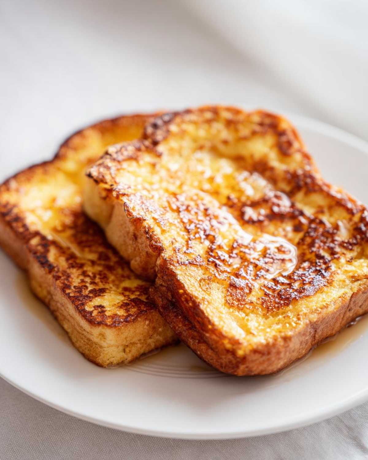 Two thick slices of golden brown french toast drizzled with syrup on a white plate.