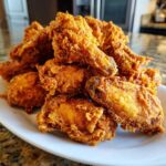 A large pile of golden brown, crispy fried chicken wings stacked high on a white plate.