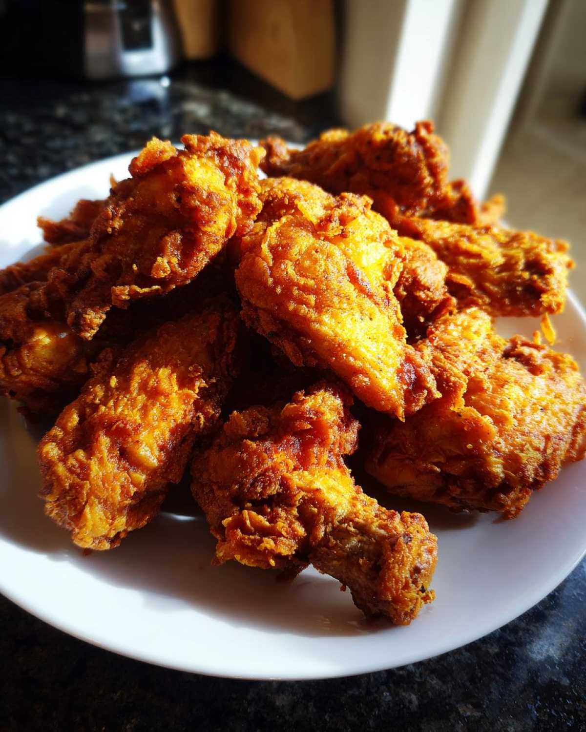 A close-up shot of a pile of golden-brown, crispy fried chicken wings served on a white plate.