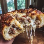 A hand holding a cross-section of amazing garbage bread with melted cheese stretching out.