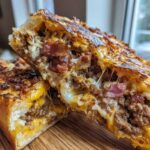 Close-up of delicious garbage bread cut in half, showing melted cheese, ground meat, and bacon filling.