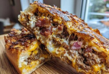 Close-up of delicious garbage bread cut in half, showing melted cheese, ground meat, and bacon filling.