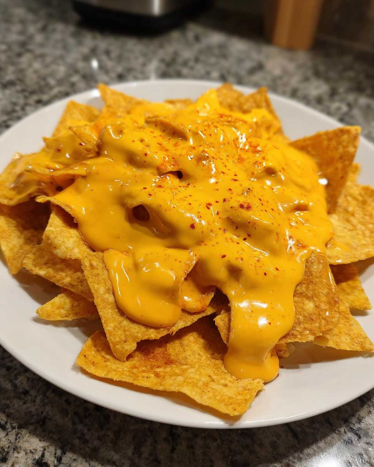 Close-up of tortilla chips generously covered in bright orange nacho cheese sauce and sprinkled with paprika.
