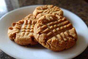Three golden brown peanut butter cookies with classic crisscross fork marks stacked on a white plate.