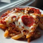 Close-up of a serving of amazing pizza pasta bake topped with melted mozzarella, pepperoni slices, and herbs.