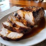 A perfectly cooked and sliced pork loin roast drizzled with a savory brown glaze on a white plate.