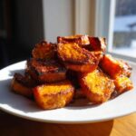 A pile of caramelized, perfectly roasted sweet potatoes with slightly charred edges on a white plate.