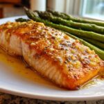 Close-up of a perfectly cooked salmon recipe fillet topped with garlic glaze, served next to bright green asparagus spears.